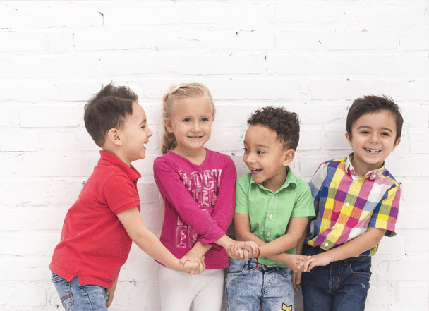 A group of children holding hands in front of a brick wall.