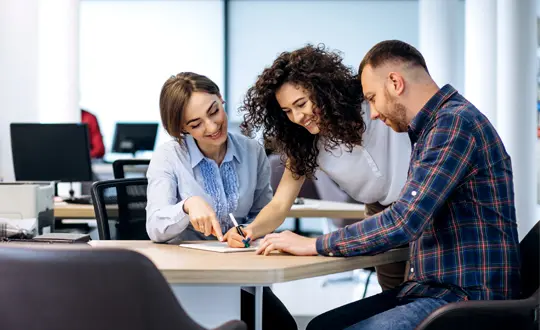 Three people sitting at a table and one is writing on paper.