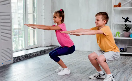 A boy and girl are doing squats in the gym.