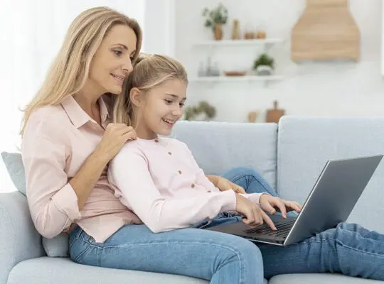 A woman and girl sitting on the couch using a laptop.