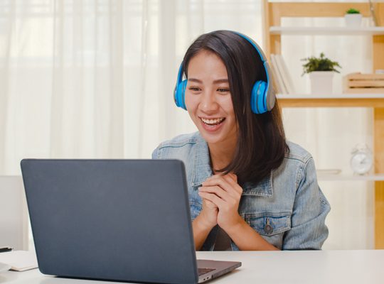 A woman with headphones on looking at her laptop.